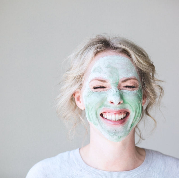 Woman with green face pack on, eyes closed and smiling