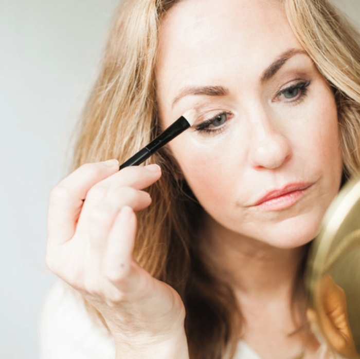 Lady looking into mirror applying eye shadow with brush